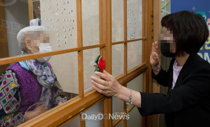 대구시에 살고 있는 A(女사진)씨가 지난 5일 동명면 바오로둥지너싱홈 요양원을 찾았다. 대면면회가 금지되어 어머님 가슴 대신에 유리창에 카네이션을 달고 있다. 사진제공 칠곡군청 공보계 박종석